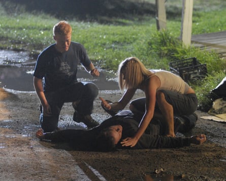 A young couple kneel beside a man lying on the ground late at night.