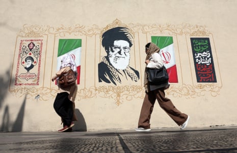 Two women walk past a Tehran mural of Ayatollah Khamenei flanked by Iranian flags