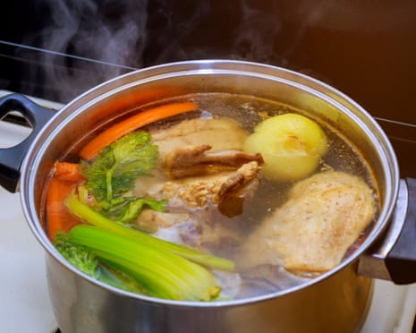 A steaming pot contains chicken pieces, carrots, celery and a potato in broth