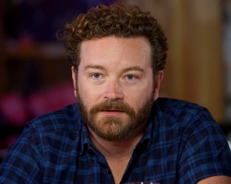 Danny Masterson, with curly hair and a beard in a plaid shirt, looks to the side