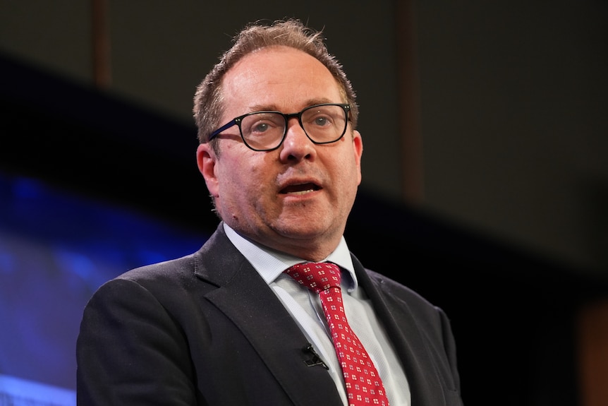 Daniel Mulino speaking while wearing dark suit with red tie and glasses.