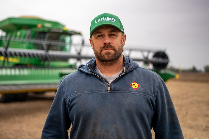 Thomsen stands in a field in front of a crop harvester.